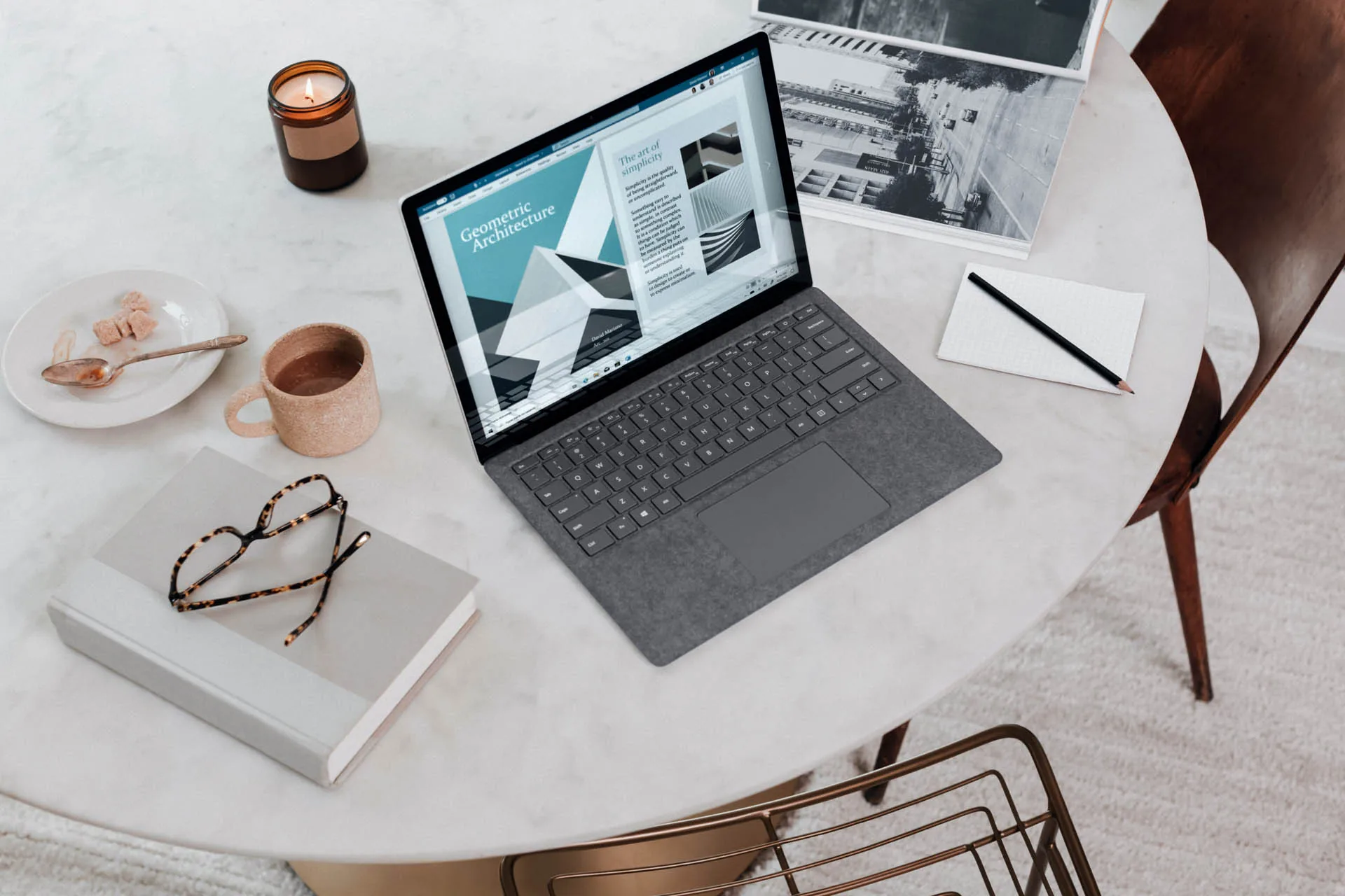 Portátil abierto sobre una mesa de trabajo junto a un cuaderno y unas gafas