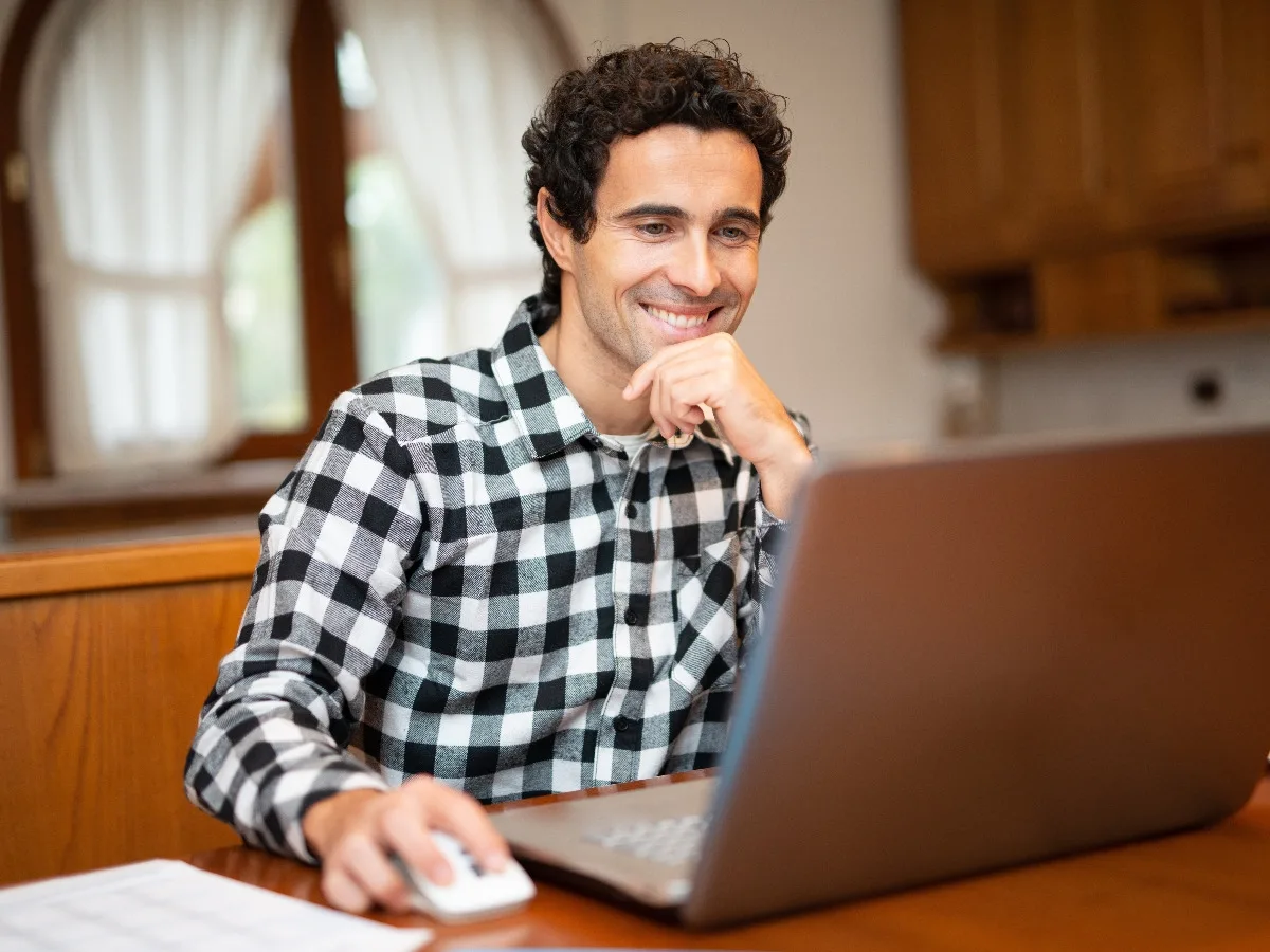Hombre sonriendo mientras consulta información en su portátil desde casa